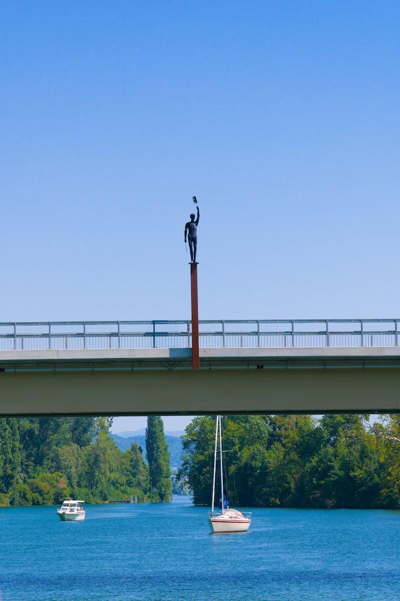 A scenic view of a statue on a bridge above the Aare River with boats and lush greenery in Switzerland.